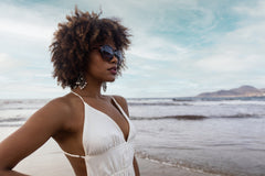 Portrait of beautiful black woman with curly hair wearing reading sunglasses on the beach.